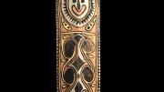 A large, colourful war shield from Kupkein, Upper Sepik. Features a smiling face with six black circles below. Front view.